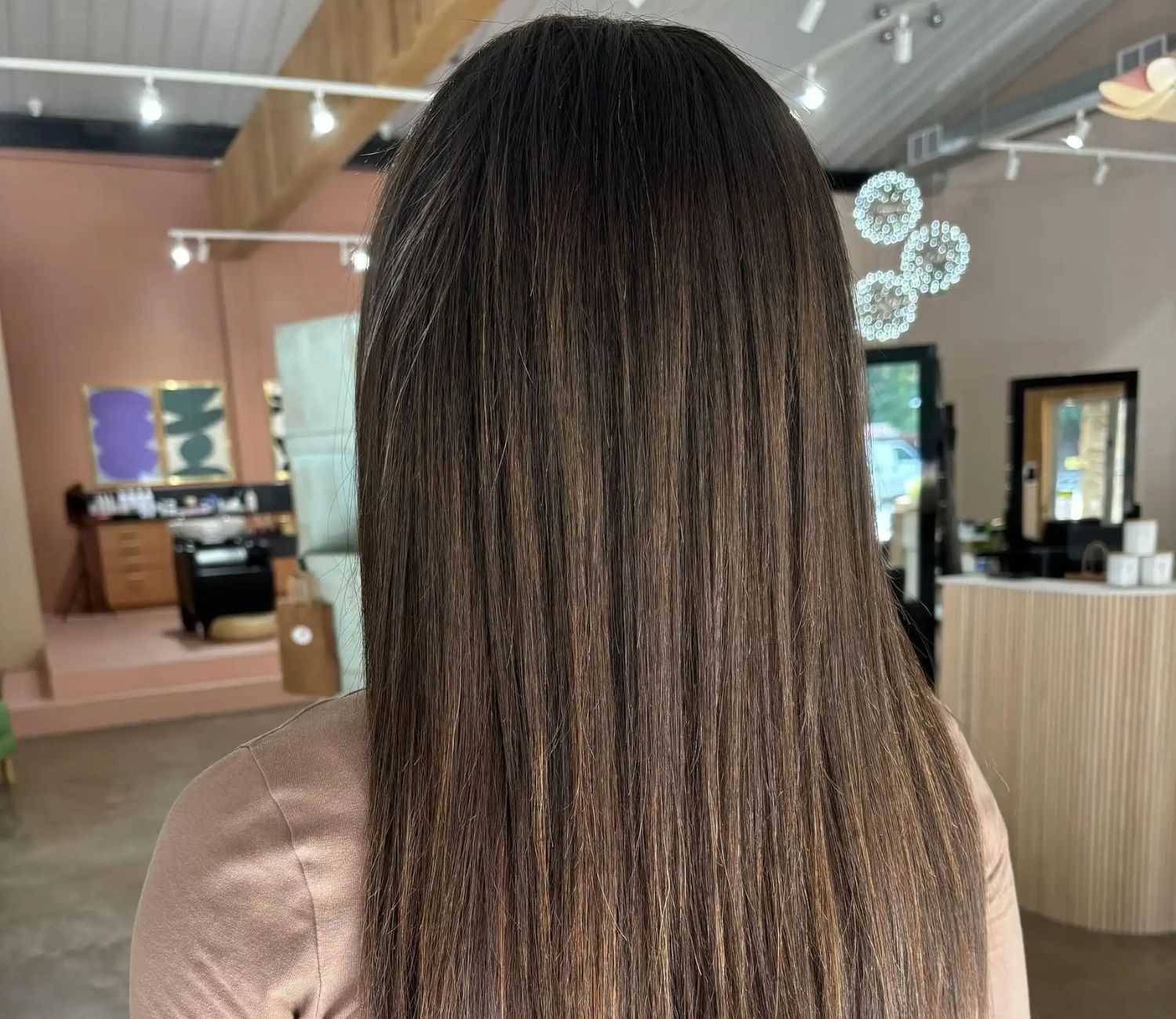Back view of a person with straight, long brown hair in a modern hair salon.